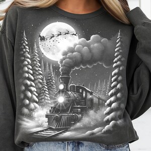 May include: Dark gray sweatshirt featuring a black and white illustration of a steam train traveling through a snowy forest at night. A full moon and Santa's sleigh are visible in the sky.