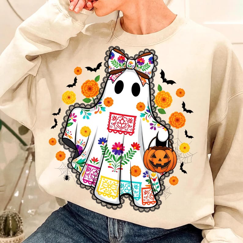 May include: Cream-colored sweatshirt featuring a ghost design with colorful floral patterns and a bow. The ghost holds a jack-o'-lantern. Orange flowers and black bats surround the ghost, creating a festive Halloween theme.