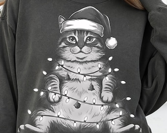 Puede incluir: Sudadera gris oscuro con un gato que lleva un gorro de Papá Noel y está envuelto en luces navideñas. El gato tiene una expresión sonriente. Las luces tienen pequeñas campanas y un solo adorno.