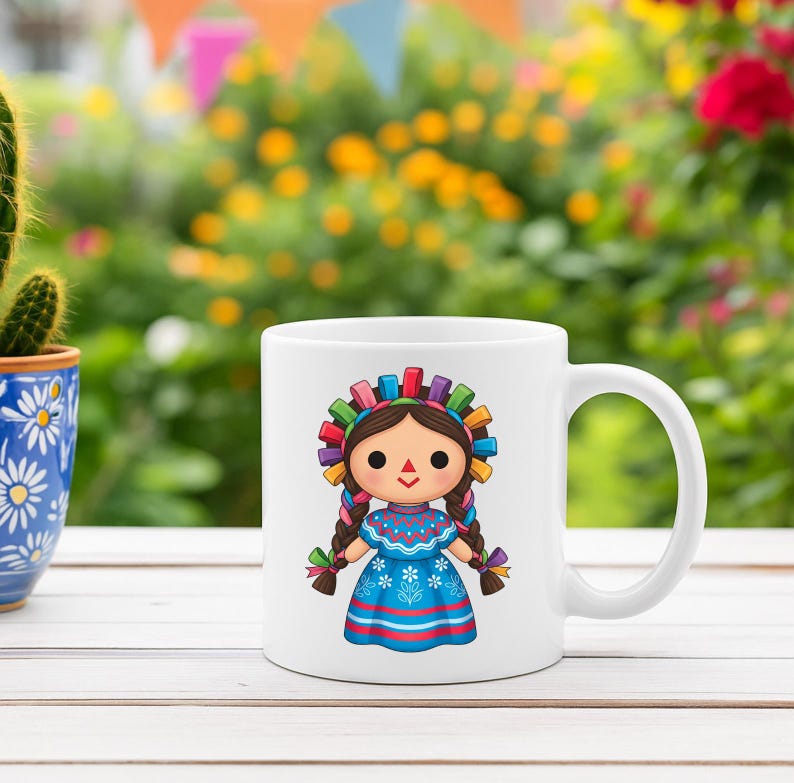K&ouml;nnte beinhalten: Wei&szlig;e Keramik-Tasse mit einer farbenfrohen Illustration einer traditionellen mexikanischen Puppe. Die Puppe hat braune Z&ouml;pfe, ein blaues Kleid und ein dekoratives Stirnband. Die Tasse steht vor einem verschwommenen Hintergrund aus Gr&uuml;n und Blumen.