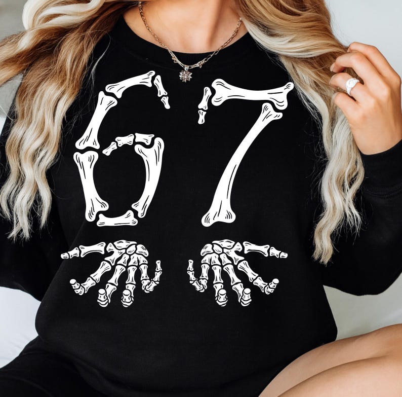 May include: Black sweatshirt with a white skeleton design. The design features the number 67 in a bone-like font, with two skeleton hands at the bottom. The sweatshirt is a crew neck style.