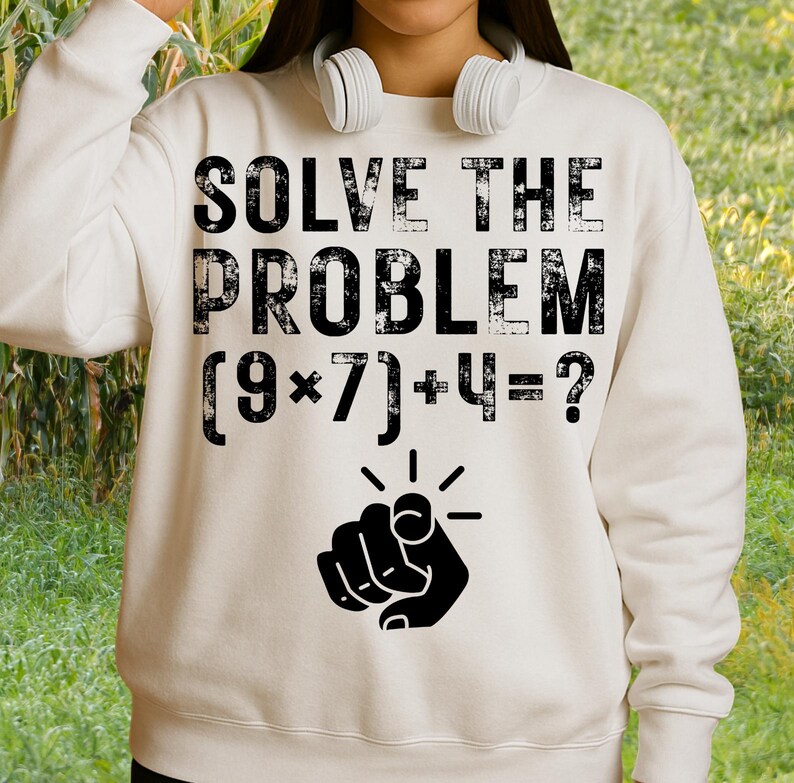 May include: Cream-colored sweatshirt with the text "SOLVE THE PROBLEM" above a math equation and a pointing finger graphic. The equation reads (9*7)+4=? The sweatshirt has a crew neck and long sleeves.