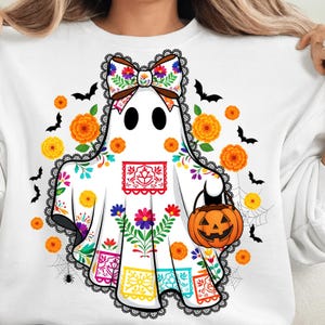 Może przedstawiać: Biała bluza z motywem Halloween z wzorem ducha z kwiatową kokardą i dynią. Duch jest ozdobiony kolorowymi kwiatami i koronkowymi wykończeniami. Czarne nietoperze, pomarańczowe kwiaty i pajęczyny dopełniają świąteczny design.