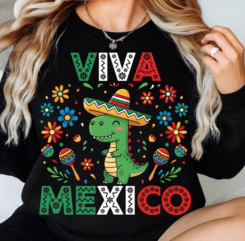Op de afbeelding: Zwart sweatshirt met een kleurrijke afbeelding van een groene dinosaurus met een sombrero. De tekst "VIVA MEXICO" is weergegeven in wit en met kleurrijke bloemmotieven. Het ontwerp bevat maracas en bloemen.