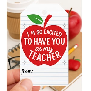 May include: A white gift tag with blue lined paper design. A red apple graphic with the text "I'M SO EXCITED TO HAVE YOU as my TEACHER" is centered on the tag. The tag also includes the word "from:" at the bottom.