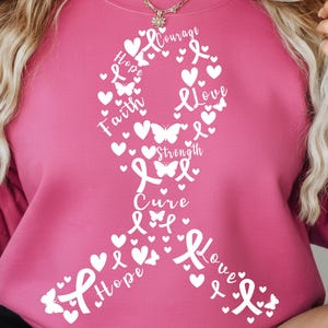 May include: Pink sweatshirt featuring a white ribbon design composed of hearts, butterflies, and the words "Hope", "Faith", "Love", "Strength", and "Cure". The design is a symbol of support and awareness.
