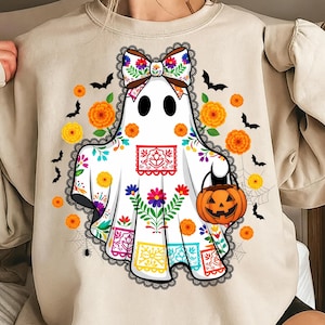May include: A beige sweatshirt featuring a white ghost with a colorful floral design and a pumpkin-shaped bag. The ghost has a decorative bow and is surrounded by orange flowers, bats, and spiderwebs, perfect for Halloween.