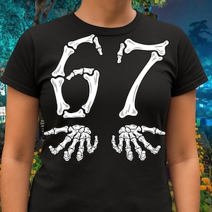 May include: Black t-shirt with a white skeleton-themed design. The design features the number "67" in a bone-like font, with two skeletal hands at the bottom. The shirt is a crew neck style.