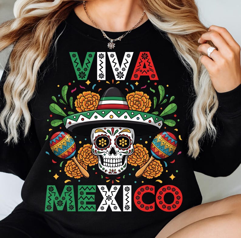 Op de afbeelding: Zwarte sweatshirt met een kleurrijk "Viva Mexico" ontwerp. De afbeelding bevat een suikerschedel met een sombrero, maracas en bloemaccenten in groen, rood en geel. De teksten "VIVA" en "MEXICO" zijn ook aanwezig.