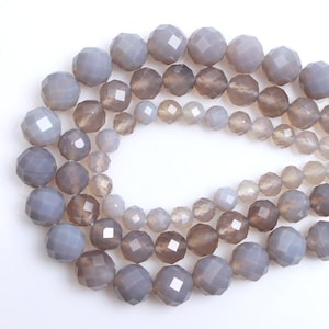 May include: Strands of faceted gemstone beads in varying shades of grey and brown. The beads are round and have a multi-faceted surface, creating a sparkling effect. The beads are strung together, ready for jewellery making.