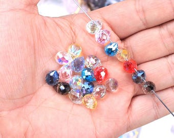 May include: Assortment of colourful faceted glass beads in various shades of blue, pink, red, and clear. The beads are approximately 8mm by 10mm in size and are strung on a wire.