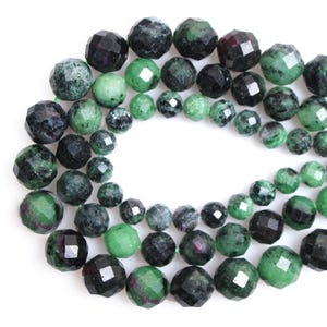 Puede incluir: Cadenas de cuentas de piedras preciosas facetadas de varios tamaños. Las cuentas muestran una mezcla de tonos verde oscuro, verde esmeralda y negro, algunas con toques de rojo. Las cuentas están ensartadas, creando una estética natural.