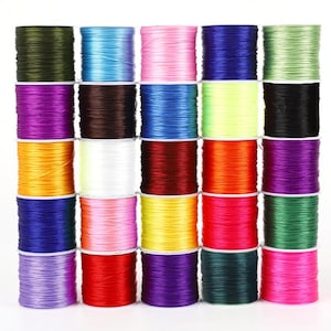 May include: A grid of colorful elastic cord spools in various shades, including green, blue, pink, purple, and orange. The spools are neatly stacked, showcasing a range of vibrant colors suitable for crafting and jewelry making.