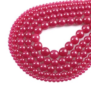 Puede incluir: Una hebra de cuentas redondas de piedras preciosas rosas de varios tamaños. Las cuentas son lisas y pulidas, con un acabado brillante.