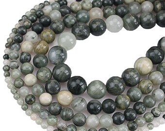 May include: A strand of green and white gemstone beads. The beads are round and have a smooth, polished finish. The beads are arranged in a circular pattern, with the largest beads in the center and the smallest beads on the outside.