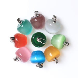 May include: A collection of colorful gemstone pendants in various shapes and hues, including green, red, pink, blue, and yellow. Each pendant has a silver-colored metal cap. The pendants are arranged in a circular pattern against a white background.