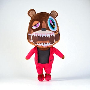 Puede incluir: Muñeco de oso de peluche con cabeza marrón y atuendo rojo. El oso tiene una cara detallada con una amplia sonrisa y ojos desiguales. El atuendo incluye una chaqueta, pantalones y zapatos rojos, con una camisa negra debajo.