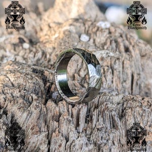 May include: A silver ring with a hammered finish and a unique, angular design. The ring is made of metal and has a polished surface.