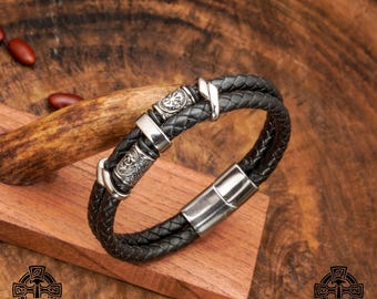 May include: A black leather bracelet with a silver magnetic clasp and decorative silver beads. The beads have Celtic knot designs.
