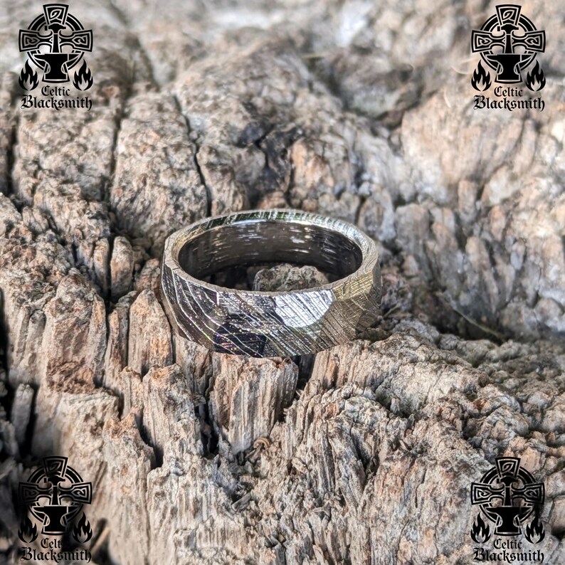 May include: A silver ring with a hammered finish. The ring is made of metal and has a textured surface. The ring is sitting on a piece of wood.