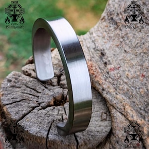 Könnte beinhalten: Ein gebürstetes silbernes Metall-Armband. Das Armband ist schlicht und modern im Design. Es wurde von Celtic Blacksmith hergestellt.