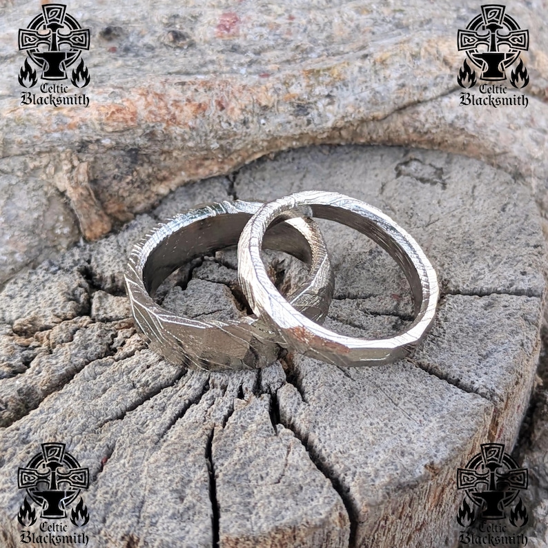 May include: Two silver wedding bands with a hammered finish, resting on a piece of weathered wood. The bands are slightly overlapping, showcasing their unique texture.