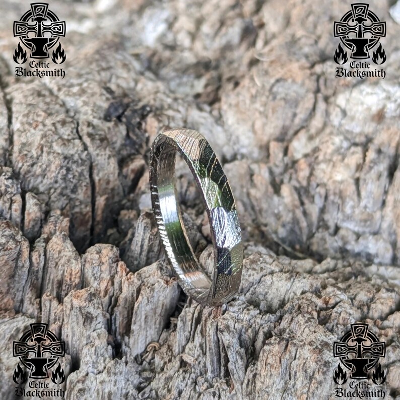 May include: A silver ring with a hammered finish and a unique, angular shape. The ring is made of metal and has a polished surface.