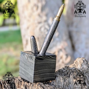 May include: A pen and pencil set in a square pen holder. The pens and holder have a distinctive, patterned design in shades of grey and black. The pen has a gold-coloured tip. The Celtic Blacksmith logo is visible in the background.