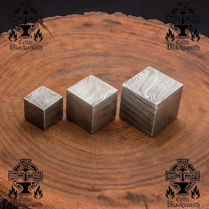 Könnte beinhalten: Drei unterschiedlich große Würfel aus gemustertem Stahl. Die Würfel sind in einer Reihe von klein nach groß auf einer Holzoberfläche angeordnet.