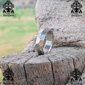 May include: A silver ring with a textured, hammered finish. The ring is made of meteorite metal and has a unique, natural pattern.