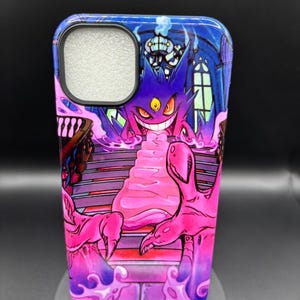 Puede incluir: Funda de teléfono con una vibrante ilustración de un personaje de dibujos animados púrpura con ojos amarillos y una amplia sonrisa, sobre un fondo de un edificio de estilo gótico. El diseño incorpora tonos de púrpura, rosa y azul.