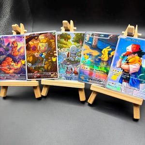 Può includere: Cinque carte collezionabili Pokémon colorate, raffiguranti personaggi come Charmander, Bulbasaur, Squirtle e Pikachu, esposte su piccoli cavalletti di legno. Le carte presentano illustrazioni dettagliate e nomi dei personaggi.