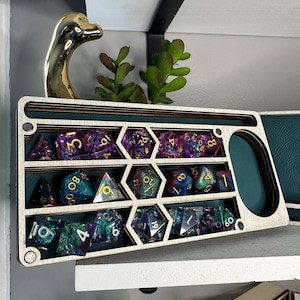 May include: A rectangular wooden dice storage tray with a teal interior, featuring multiple hexagonal and rectangular compartments filled with assorted multi-colored glittery polyhedral dice with gold and white numbering.