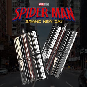 Op de afbeelding: Twee zilveren en rode Spider-Man web shooters met een stadsachtergrond. Het Marvel Studios-logo en de woorden "SPIDER-MAN" in rood en blauw, en "BRAND NEW DAY" in geel staan erboven.
