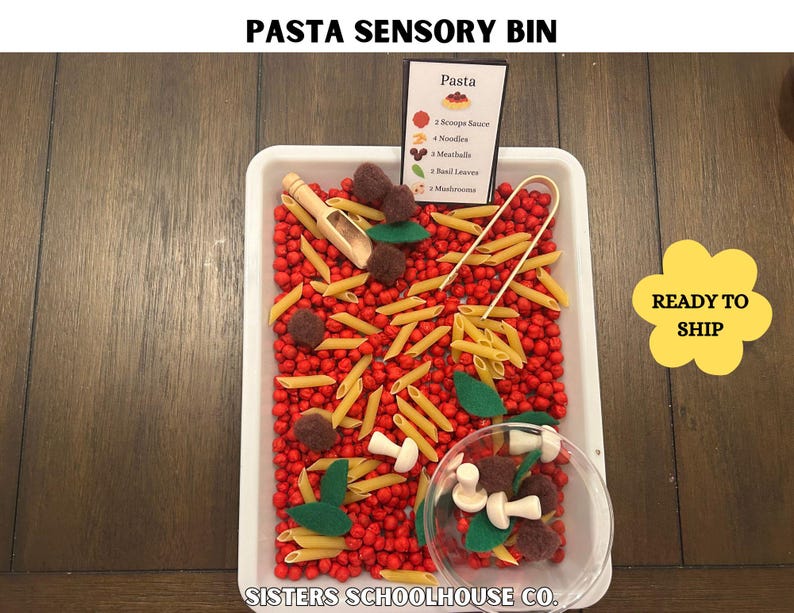 Puede incluir: Un recipiente sensorial de pasta con cuentas rojas, pasta penne, alb&oacute;ndigas de fieltro, champi&ntilde;ones y hojas de albahaca. Incluye una peque&ntilde;a cuchara de madera y un recipiente transparente con ingredientes de pasta. El recipiente tiene un letrero que dice "Pasta".