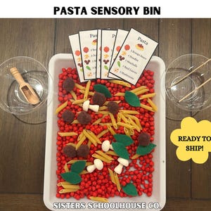 Puede incluir: Un recipiente sensorial etiquetado como "PASTA SENSORY BIN" lleno de cuentas rojas, pasta penne, hojas de fieltro y alb&oacute;ndigas de fieltro. Incluye cuencos peque&ntilde;os, una cuchara de madera y pinzas. El recipiente tiene tarjetas con una receta de pasta.