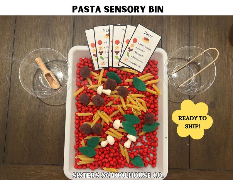 Puede incluir: Un recipiente sensorial etiquetado como "PASTA SENSORY BIN" lleno de cuentas rojas, pasta penne, hojas de fieltro y alb&oacute;ndigas de fieltro. Incluye cuencos peque&ntilde;os, una cuchara de madera y pinzas. El recipiente tiene tarjetas con una receta de pasta.