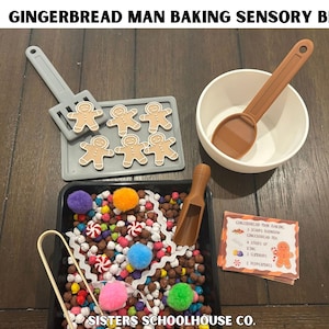 May include: A gingerbread man baking sensory bin set including a gray tray with six gingerbread figures, a white bowl with a brown scoop, a black bin filled with colorful pom-poms and small brown spheres, a brown scoop, tongs, and a recipe card.