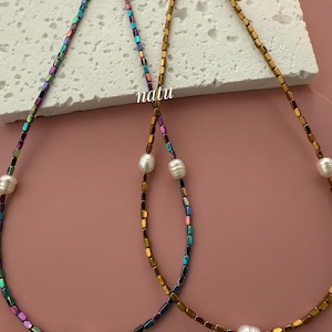 Peut inclure: Deux colliers avec des perles carrées irisées et des accents de perles blanches. Le collier de gauche a une finition irisée arc-en-ciel, tandis que le collier de droite a une finition irisée dorée.