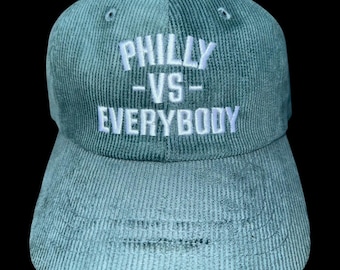 May include: A teal corduroy baseball cap with the text "PHILLY -VS- EVERYBODY" embroidered in white. The cap has a curved brim and a structured crown, suitable for casual wear.