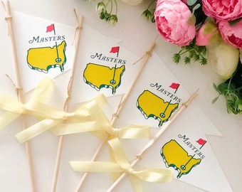Può includere: Quattro bandiere bianche con disegni di campi da golf gialli e verdi e la parola "Masters" stampata su ciascuna. Le bandiere sono attaccate a bastoni di legno con fiocchi di nastro giallo.