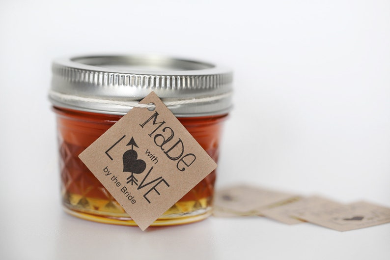 Puede incluir: Un peque&ntilde;o frasco de vidrio lleno de un l&iacute;quido dorado, con una etiqueta de papel marr&oacute;n atada alrededor de la tapa. La etiqueta dice "Made with LOVE by the Bride".