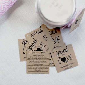 Puede incluir: Un conjunto de etiquetas de regalo de papel marr&oacute;n con texto negro y un dise&ntilde;o de coraz&oacute;n. Las etiquetas dicen "Spread the Love" y "Wanda & Mark 09.01.2012".