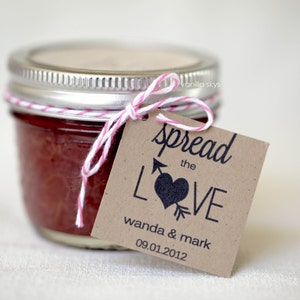 Puede incluir: Un peque&ntilde;o tarro de vidrio lleno de mermelada roja, atado con un lazo de cuerda rosa y blanca. Una etiqueta de papel marr&oacute;n est&aacute; unida con el texto "spread the LOVE wanda & mark 09.01.2012"