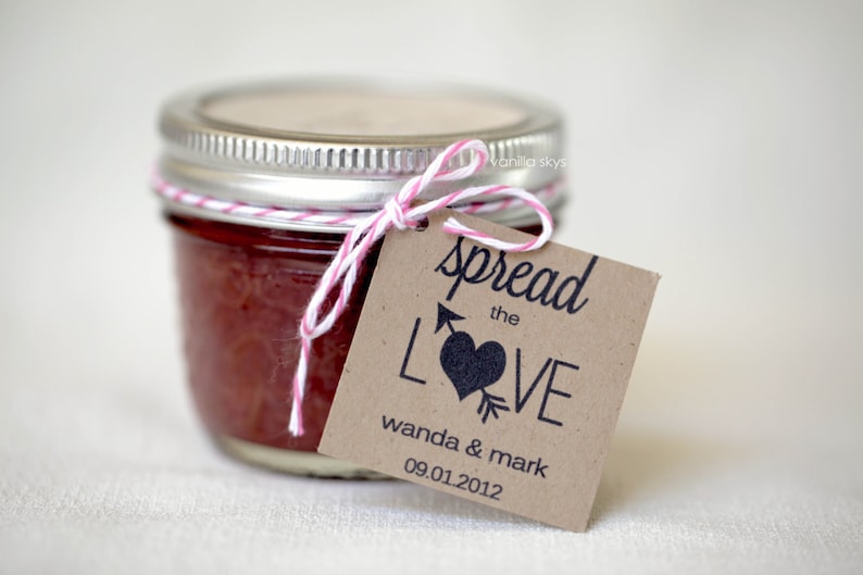 Puede incluir: Un peque&ntilde;o tarro de vidrio lleno de mermelada roja, atado con un lazo de cuerda rosa y blanca. Una etiqueta de papel marr&oacute;n est&aacute; unida con el texto "spread the LOVE wanda & mark 09.01.2012"