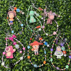 K&ouml;nnte beinhalten: Eine Sammlung von Schl&uuml;sselanh&auml;ngern mit Charakteren aus dem Animationsfilm Toy Story. Jeder Schl&uuml;sselanh&auml;nger hat einen Charakteranh&auml;nger, bunte Perlen und einen Metallring. Zu den Charakteren geh&ouml;ren Woody, Rex, Bullseye, Lotso, Jessie und Buzz Lightyear.
