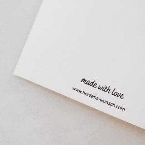 Puede incluir: Una tarjeta blanca con el texto "made with love" y la direcci&oacute;n del sitio web www.herzens-wunsch.com impresos en negro. La tarjeta est&aacute; en &aacute;ngulo, mostrando una esquina y el borde del papel.