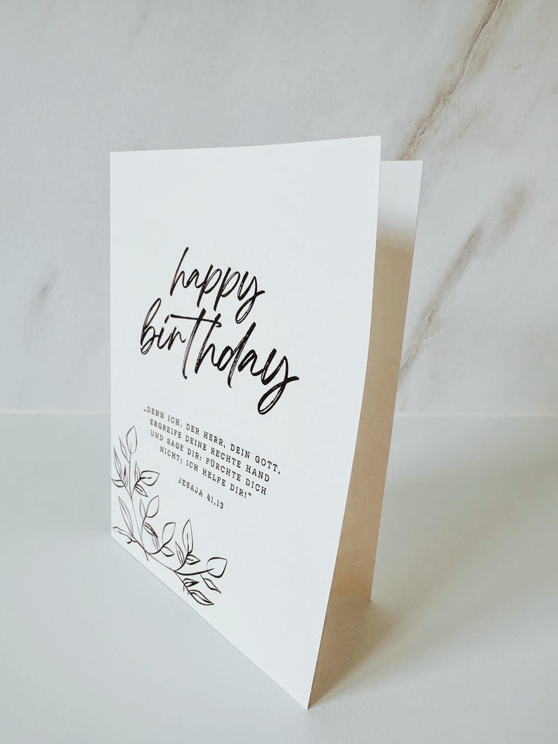 Puede incluir: Una tarjeta de cumplea&ntilde;os blanca con las palabras "happy birthday" en elegante escritura negra. La tarjeta tambi&eacute;n presenta una cita en alem&aacute;n y un delicado dise&ntilde;o floral. La tarjeta est&aacute; doblada y se mantiene en posici&oacute;n vertical.