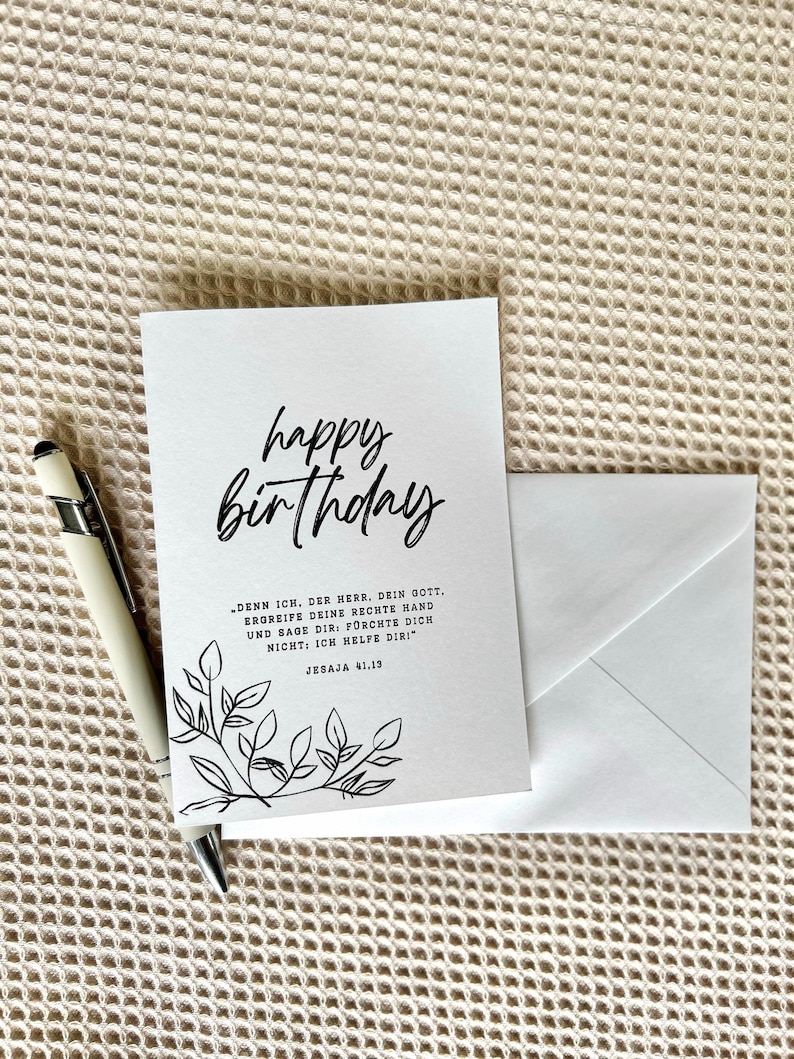 Puede incluir: Una tarjeta de cumplea&ntilde;os blanca con las palabras "happy birthday" en escritura negra. La tarjeta tiene un dise&ntilde;o floral y una cita en alem&aacute;n. Un sobre blanco y un bol&iacute;grafo est&aacute;n al lado de la tarjeta.