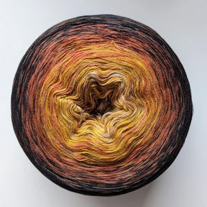 May include: A round ball of yarn with a gradient color scheme, transitioning from black to orange, yellow, and white in the center. The yarn is tightly wound, creating a spiral pattern. Ideal for knitting and crochet projects.